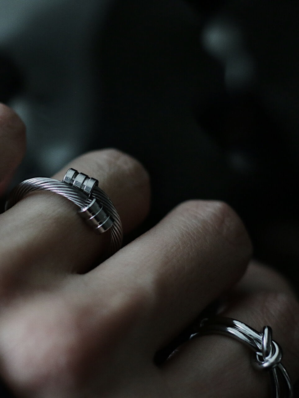 On-model photo of the adjustable stainless steel cable ring worn on an index finger, demonstrating flexible fit and industrial style. Styled alongside other silver stackable rings on a hand.