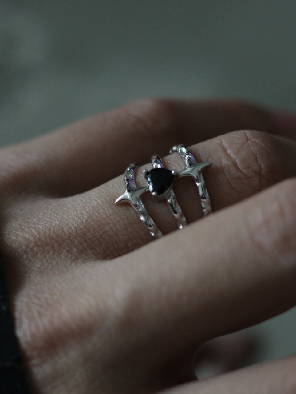 Gothic black heart zircon ring styled on finger, liquid metal silver texture, streetwear aesthetic jewelry by Monora Studio.