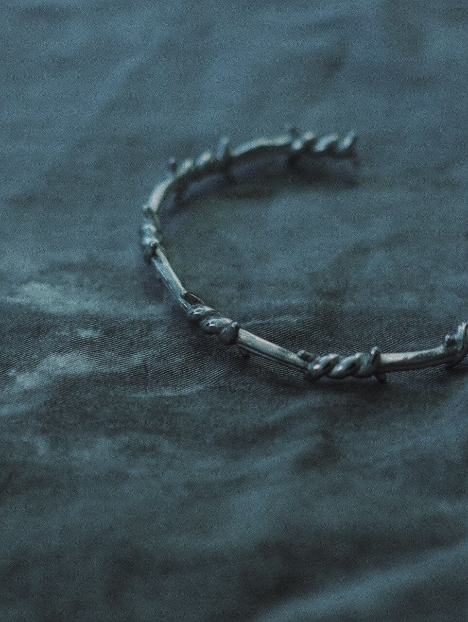 Industrial gothic silver thorn bracelet laid diagonally on a textured dark background aesthetic shot