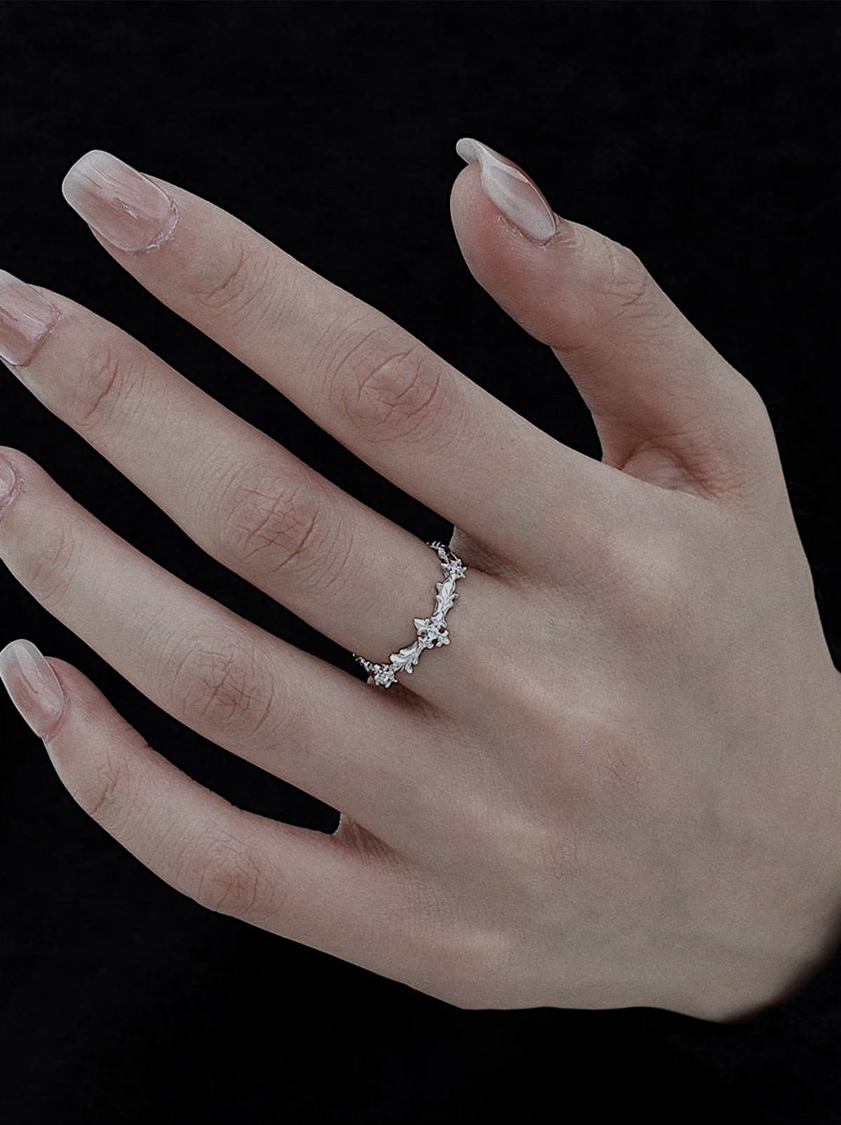 silver floral ring with zircon details on white stone background, dainty flower band on hand, sterling silver botanical ring close-up