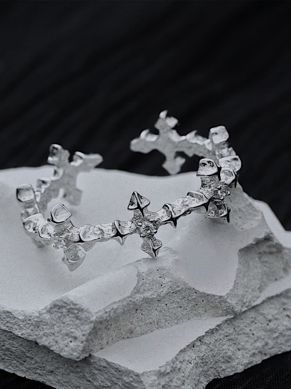 distressed silver cross ring with jagged edges, edgy gothic cross ring worn on hand, close-up of textured open band silver ring, rebel-style silver ring with rugged cross pattern