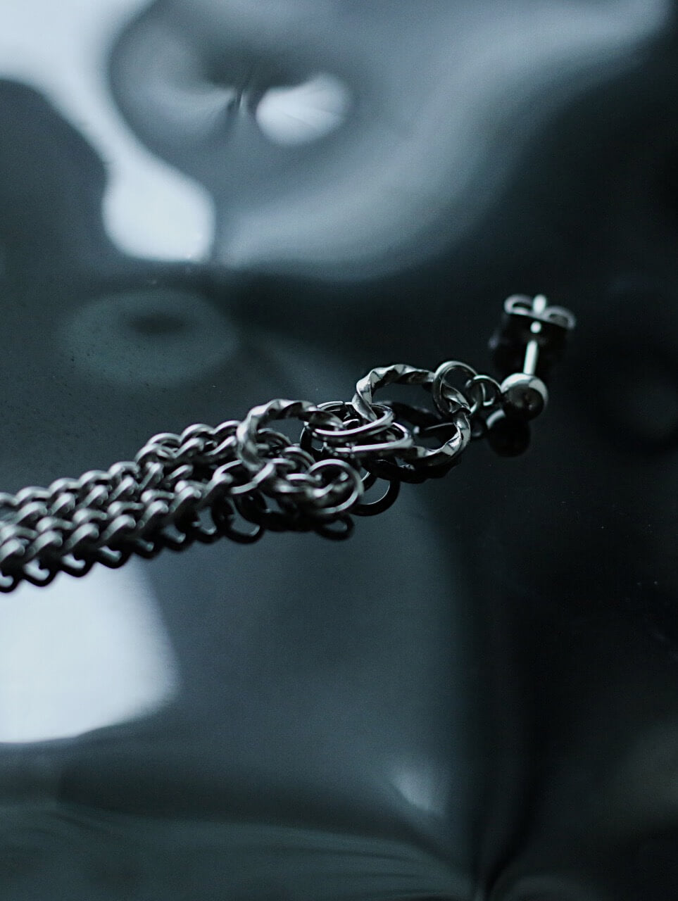 Macro cinematic shot of silver tassel chains on a reflective dark water-like surface, tarnish-proof hypoallergenic surgical steel jewelry.