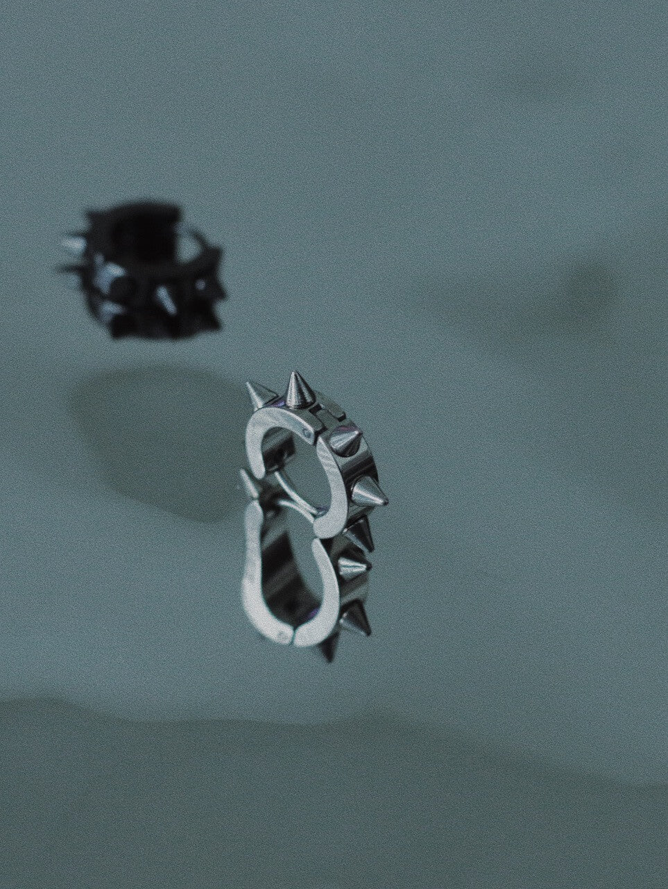 Polished silver and black stainless steel spiked huggie earrings on dark surface, durable alternative fashion accessories