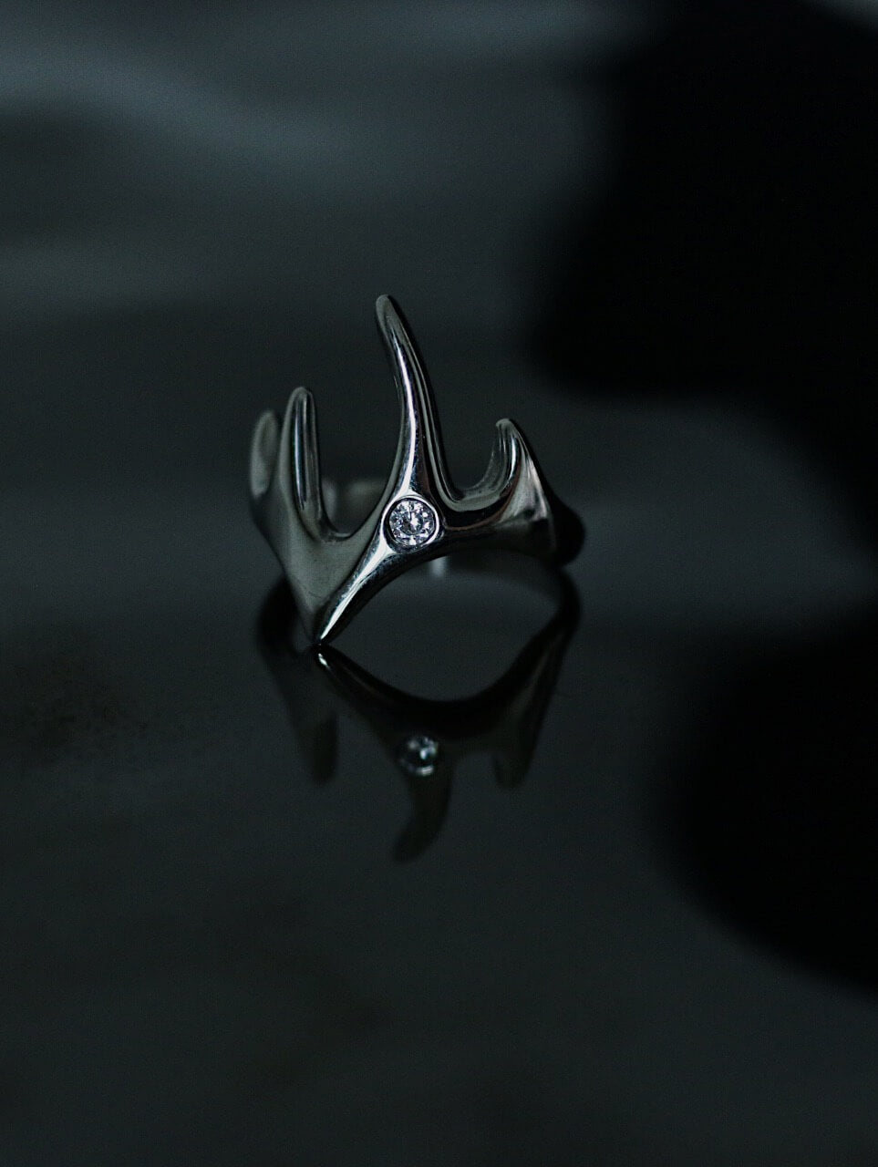 Tarnish-proof silver flowing flame ring on a dark reflective surface, high-shine industrial aesthetic jewelry, durable surgical steel.