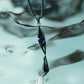 Monora Studio liquid flame shard necklace hanging vertically over a reflective glass background⁠