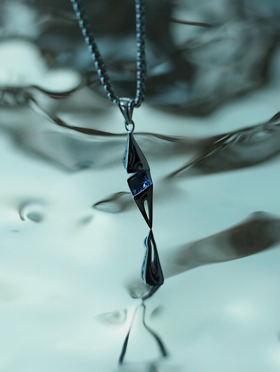 Monora Studio liquid flame shard necklace hanging vertically over a reflective glass background⁠