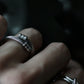 On-model photo of the adjustable stainless steel cable ring worn on an index finger, demonstrating flexible fit and industrial style. Styled alongside other silver stackable rings on a hand.