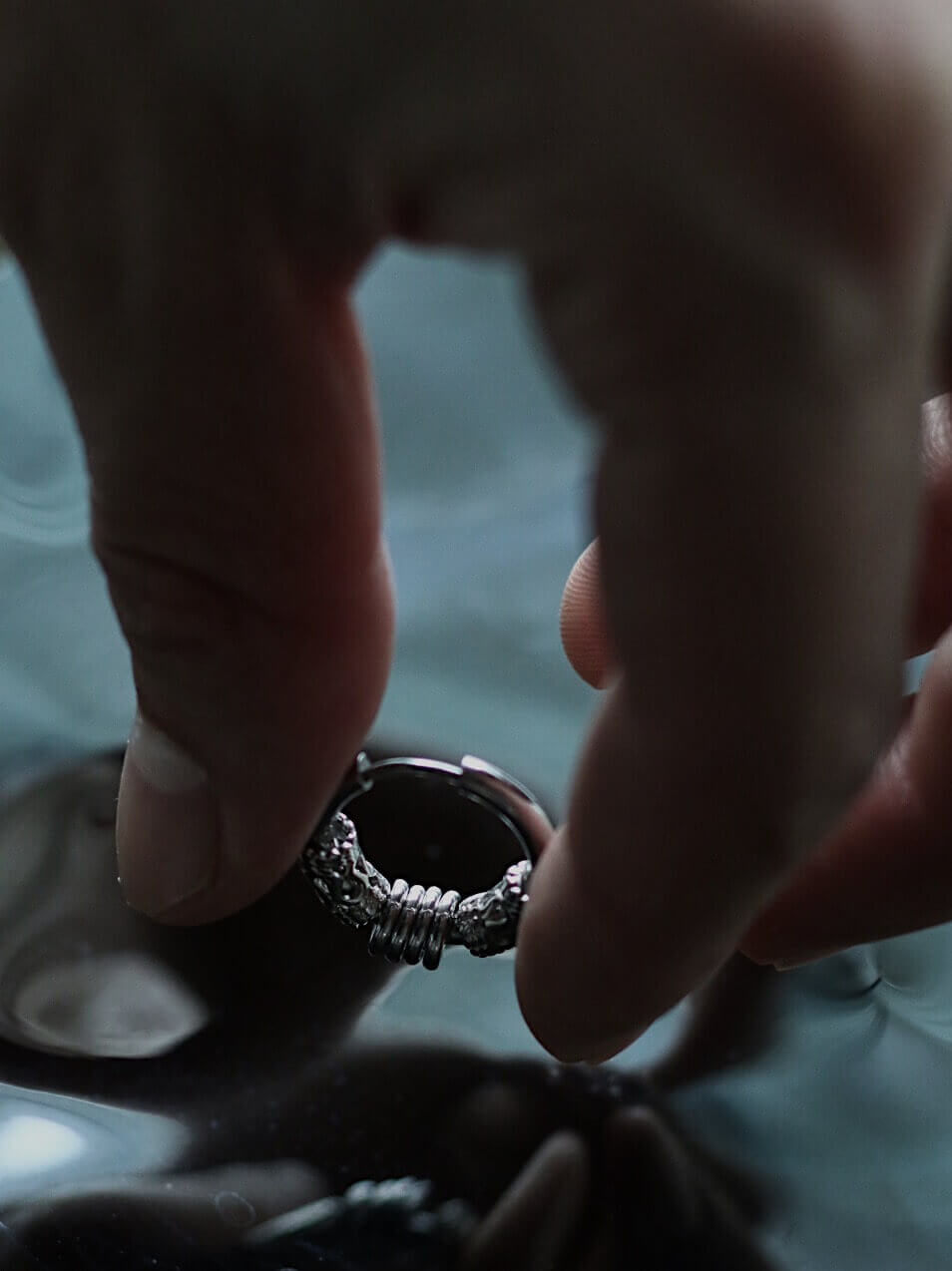 Moody cinematic shot of a tarnish-proof silver gothic hoop earring, aesthetic punk rock jewelry on black reflective surface, hypoallergenic surgical steel.