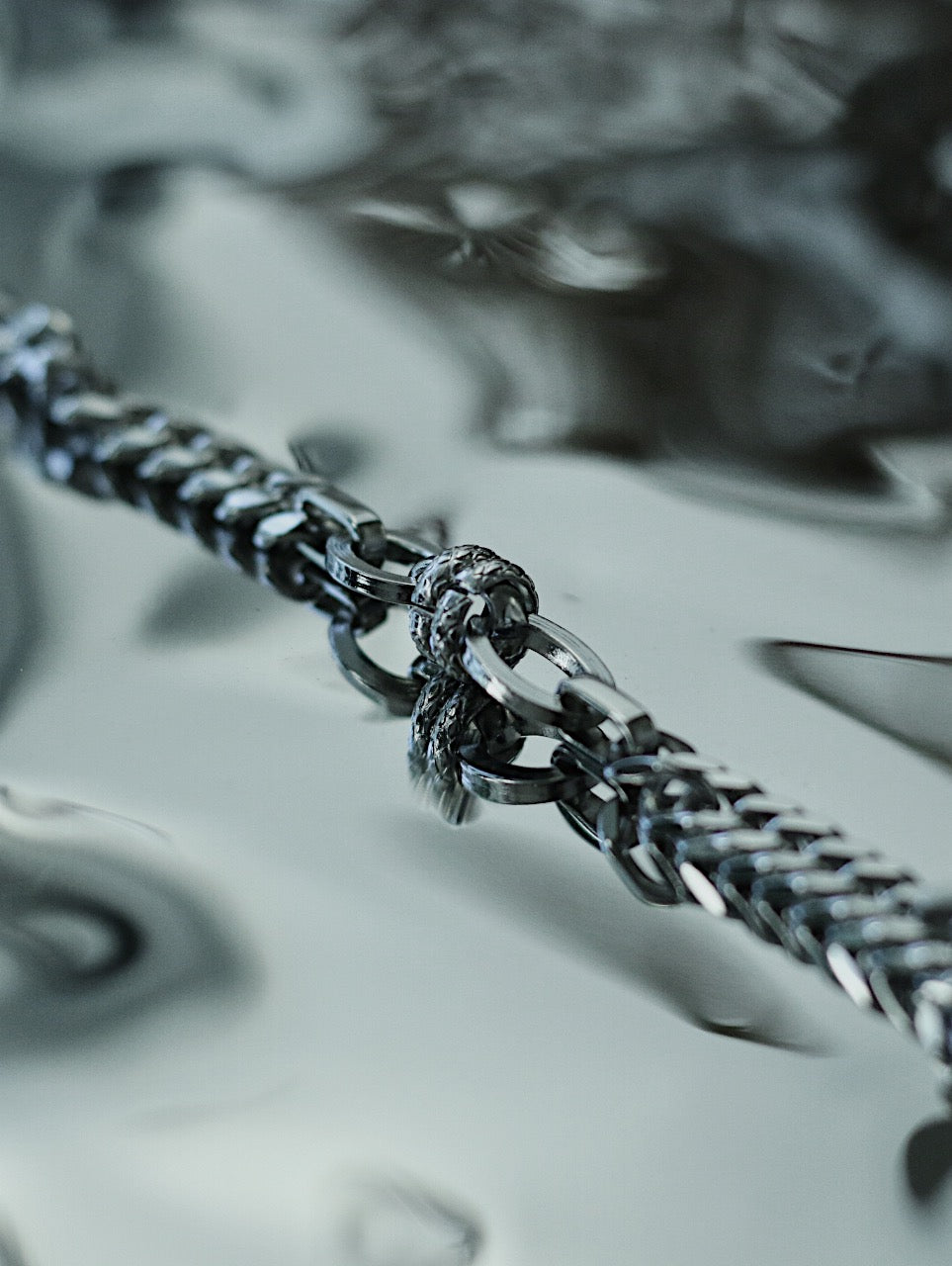Macro close up shot of Monora Studio durable titanium steel entwined link curb chain bracelet on reflective background⁠