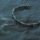 Industrial gothic silver thorn bracelet laid diagonally on a textured dark background aesthetic shot⁠