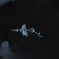 Gothic sacred wing earrings on dark reflective water surface, tarnish-proof surgical steel blade jewelry, aesthetic divine protection amulet.