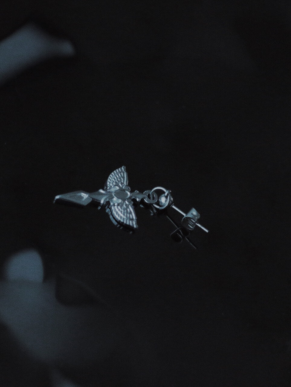 Gothic sacred wing earrings on dark reflective water surface, tarnish-proof surgical steel blade jewelry, aesthetic divine protection amulet.