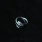 High-end product shot of the stainless steel cable bypass ring on a moody black background with realistic reflection, premium tarnish-proof silver wire ring, unisex streetwear accessory.