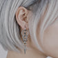 Model with silver hair wearing Monora Studio stainless steel industrial woven chain spike drop earring close up⁠